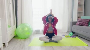 Afro-Amerikan kadın hippi renkli spor kıyafetleri ve kıvırcık afro saçlarıyla lotus pozu ve meditasyonlarda oturuyor.