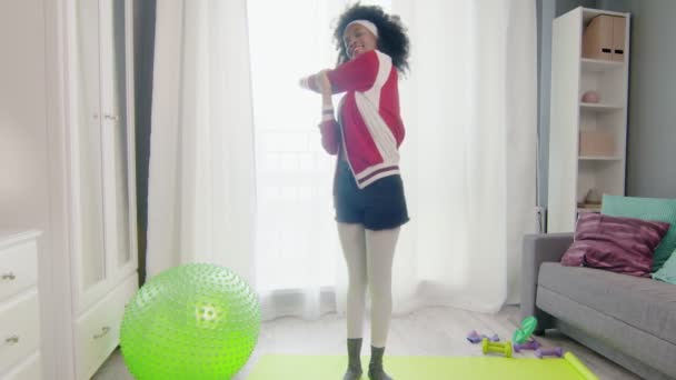 Young happy african american woman hippy in colourful sportswear with curly afro hairs looks at the camera and does stretch exercise — Stock Video