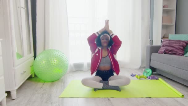 Tânăra femeie africană americană hippy în îmbrăcăminte sportivă colorată cu fire de păr creț afro stă în poziția de lotus și meditații — Videoclip de stoc