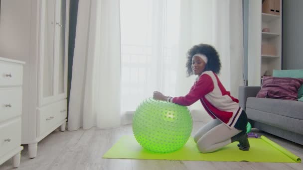 Young african american woman hippy in colourful sportswear with curly afro hairs looks at the camera and does sexy exercise — Stock Video