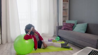 Kıvırcık saçlı, renkli spor giysili genç Afrikalı Amerikalı hippi kadın antrenmandan sonra dinleniyor.