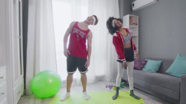 Neşeli beyaz erkek ve Afrikalı Amerikalı kadın retro modeller odada dikilirken kaslarını esnetiyorlar.