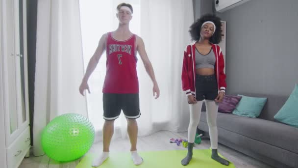 Cheerful Caucasian male and african american female retro style models stretching muscles while standing in room — Stock Video