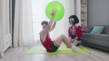 Kafkas erkek ve afro kadının evde iş yaptığı komik bir retro tarzı. Karın kasları egzersizi yapan komik bir adam. Evde spor topuyla antrenman yapıyor. Eşiyle, spor mizahıyla..