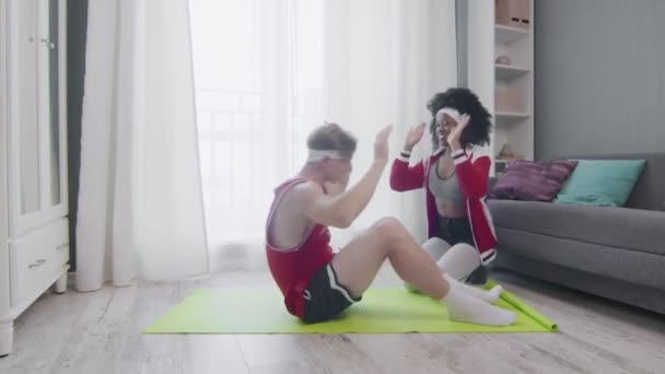 Funny retro style couple of Caucasian man and afro woman doing work up at home. Funny man doing abs exercises crunches at home with wife, fitness humor. — Stock Video