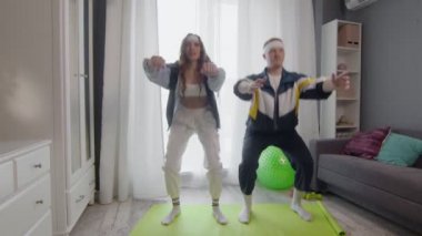 Mutlu, genç ve sağlıklı çift evde çalışıyor. Çömelme egzersizi yapıyorlar.