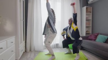 Mutlu, genç ve sağlıklı çift evde çalışıyor. Çömelip, dambılları kaldırıyorlar.