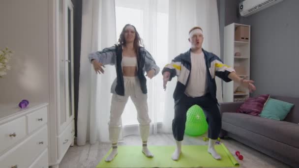 Lucu pasangan muda yang sehat pria dan wanita bekerja di rumah. Mereka melakukan latihan squat — Stok Video