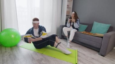Erkek arkadaşı dambılla dönüşümlü egzersiz yaparken, geriye dönük stil genç bir kadının pizza yemesini yakınlaştır