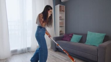 Mutlu ve neşeli genç bayan yerleri paspasla temizliyor ve telefonda konuşuyor.