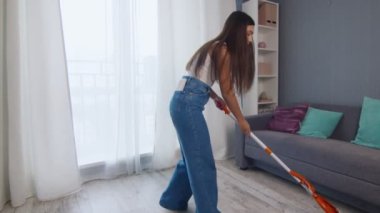 Mutlu ve neşeli genç bayan yerleri paspasla temizliyor ve telefonda konuşuyor.