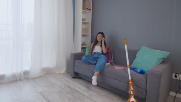 혼자서 집을 청소 한 후 피곤 한 젊은 여자가 코치 위에 앉아 전화를 사용 한다 — 비디오