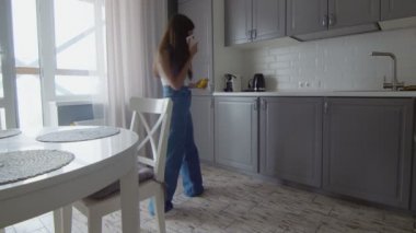 Genç bir kadın telefonla konuşuyor ve mutfağı temizlemek için sarı bez kullanıyor.