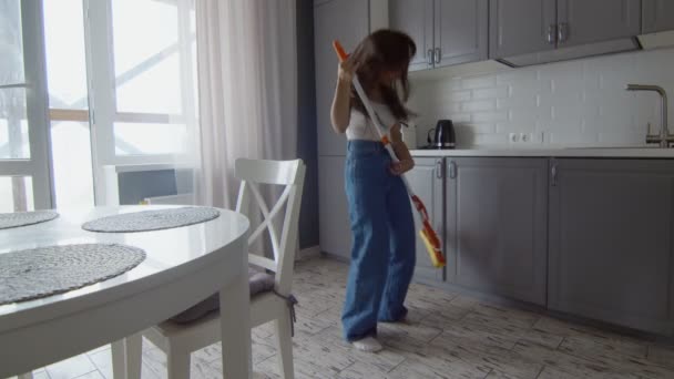 Szczęśliwa i wesoła młoda piękna kobieta sprząta podłogę i tańczy mopem jak na gitarze — Wideo stockowe