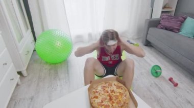 Yerde mekik çeken komik görünüşlü sporcu masadaki taze sıcak pizzaya ulaşmaya çalışıyor. Evde spor faaliyetleri.