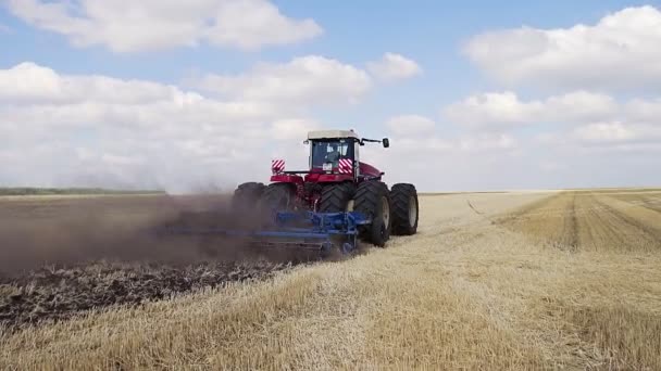 Egy piros traktor hátrameneti ekével szántja a mezőt.. — Stock videók