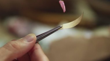 Adam küçük kağıt parçasına pembe boya sürmek için fırça kullanıyor.