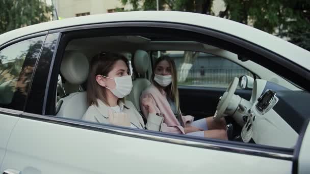 Tow 젊은 여성들은 COVID-19 확산을 막기 위해 얼굴에 의료 마스크를 쓰고 차에 앉아 있습니다.. — 비디오