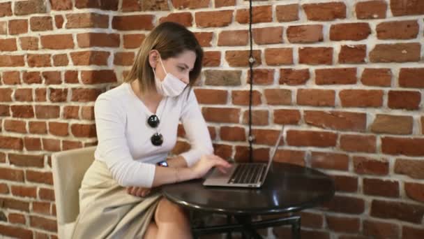 Jonge zakenvrouw in beschermende masker werkt op notebook in cafe — Stockvideo