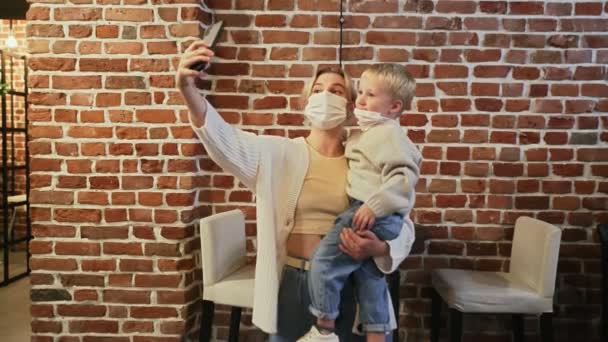 Мальчик и его мать в защитных масках делают селфи, пока ждут своего заказа в кафе — стоковое видео