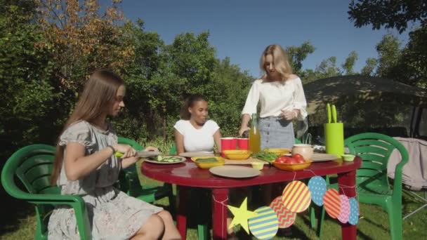 Young women set the table, cuts vegetables and pours drinks — Stock Video