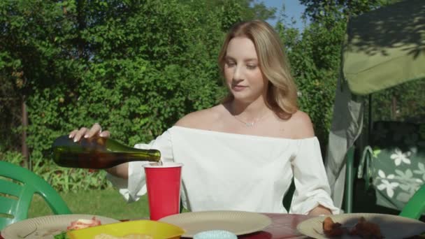 Młoda kobieta wlewa napój do papierowej filiżanki i pije na świeżym powietrzu BBQ party — Wideo stockowe