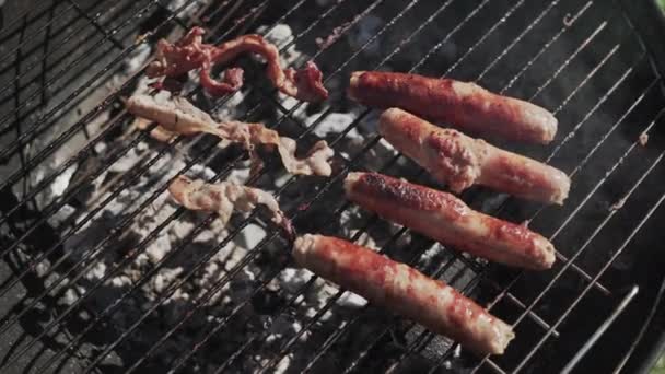 Cooking grilling bacon and sausages on bbq grid outdoors for friends picnic party — Stock Video