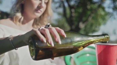 Genç bir kadın kağıt bardağa soda doldurup açık havada BQ partisinde içiyor.