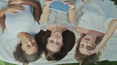 Üç kadının battaniyeye uzandığı ve yaz parkında selfie çektiği en iyi manzara.