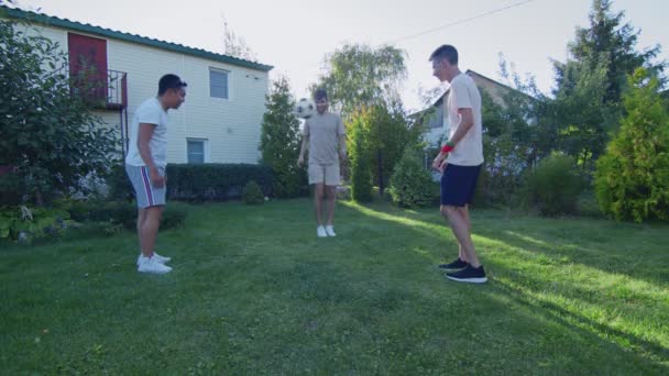 Три друзі грають з м'ячем на задньому дворі в літній час — стокове відео