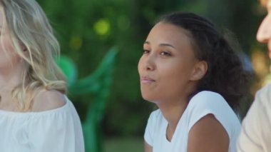 Arkadaşlarıyla şarkı söyleyen Afrikalı Amerikalı kadını yakından çek. Bir grup arkadaş parkta bir battaniyeye oturur.