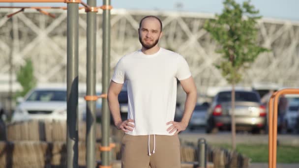 Portré fiatal atléta férfi fehér pólóban csinál bemelegítő gyakorlatok a szabadban — Stock videók