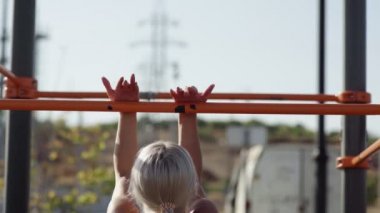 Genç bayan sporcu kendini yatay çubuğa çekiyor. Açık havada. Egzersiz