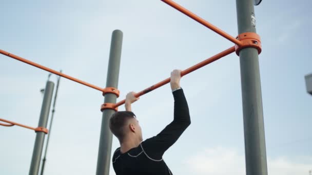 Rückenansicht eines jungen, muskulösen Mannes beim Muscle Up-Training am Barren im Freien — Stockvideo