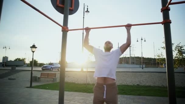 Homem jovem musculoso fazendo pull-ups na barra horizontal. Na área de treino perto de casa — Vídeo de Stock