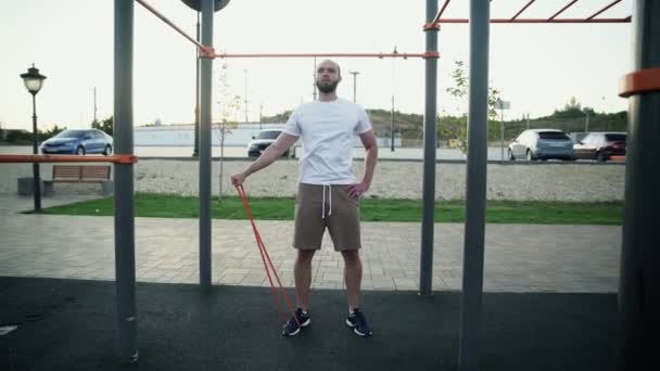 Young muscular man doing exercise to lifting right hand with stretching an elastic band outdoors. Workout — Stock Footage Young muscular man doing exercise to lifting right hand with stretching an elastic band outdoors. Workout Royalty Free Stock Footage