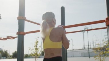 Genç bayan sporcu kendini yatay çubuğa çekiyor. Açık havada. Egzersiz