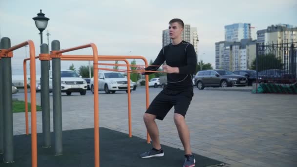 Молодий м'язистий чоловік виконує вправи з еластичною смугою на відкритому повітрі. Тренування — стокове відео