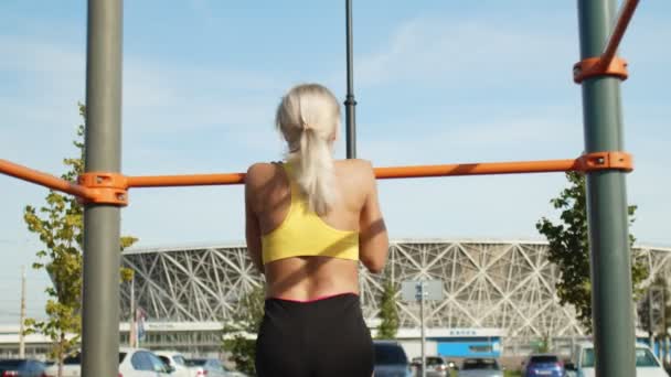 Achteraanzicht van jonge vrouwelijke atleet trekt zich omhoog op de horizontale balk. Buiten. Trainen — Stockvideo