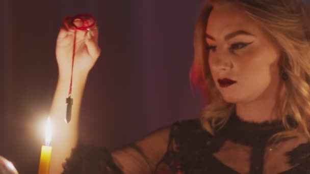 Dekat dengan peramal wanita memegang pendulum ajaib di atas lilin — Stok Video