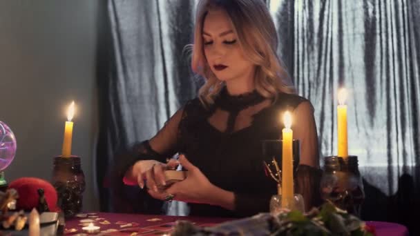 Jovem cartomante à mesa à luz das velas lê o futuro nas cartas na fumaça — Vídeo de Stock