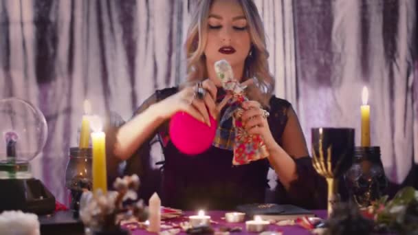 Dunkle magische Voodoo-Hexe, die Rituale durchführt und zauberhafte Piercing-Puppe mit Nadeln in dunklen Raum mit brennenden Kerzen sitzt. — Stockvideo