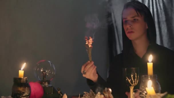 En manlig spåman i en magisk salong tänder rökelse och börjar röra hand för paranormala ritualer — Stockvideo