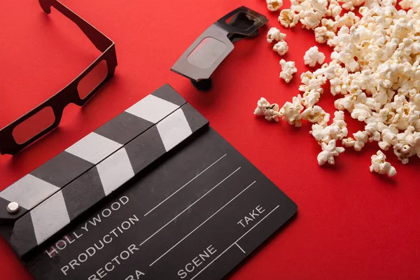 Clapperboard, óculos 3D e pipoca sobre fundo vermelho — Fotografia de Stock