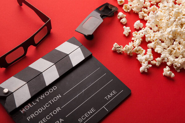 Clapperboard, 3D glasses and popcorn on red background