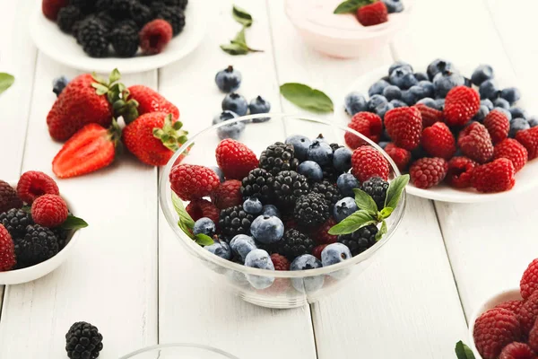 Mixed berries in glass bowls on white wooden table
