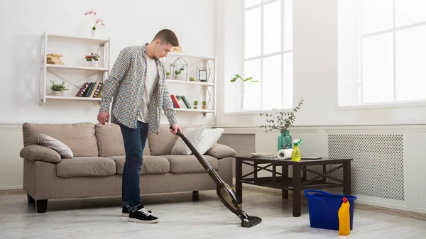 Молодой человек уборка дома с пылесосом — стоковое фото