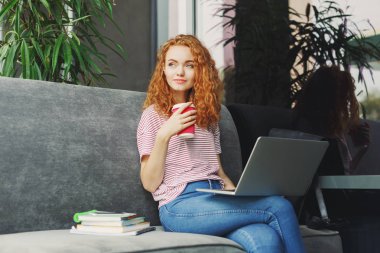 Kafede dizüstü bilgisayar kullanan mutlu genç kadın