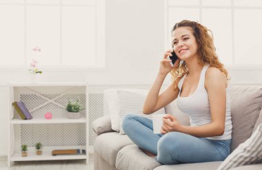 Arama mobil bej kanepede oturan genç Kızıl saçlı kadın. Telefon ve kahve içme, geri kalanı evimde üzerinde konuşmak kız gülümseyerek, kopyalama alanı