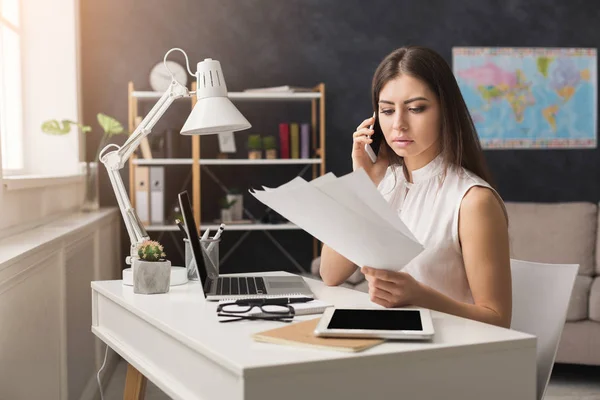 Girl at home working on laptop and talking on mobile — Stock Photo, Image